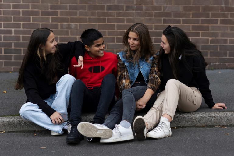 a group of friends 3 girls and 1 boy sitting on a curb chatting.