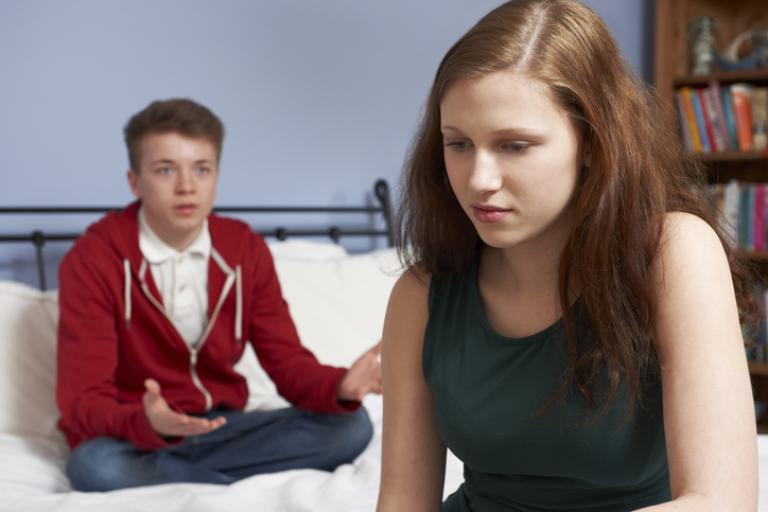 Teen couple sat in a bedroom experiencing relationship problems